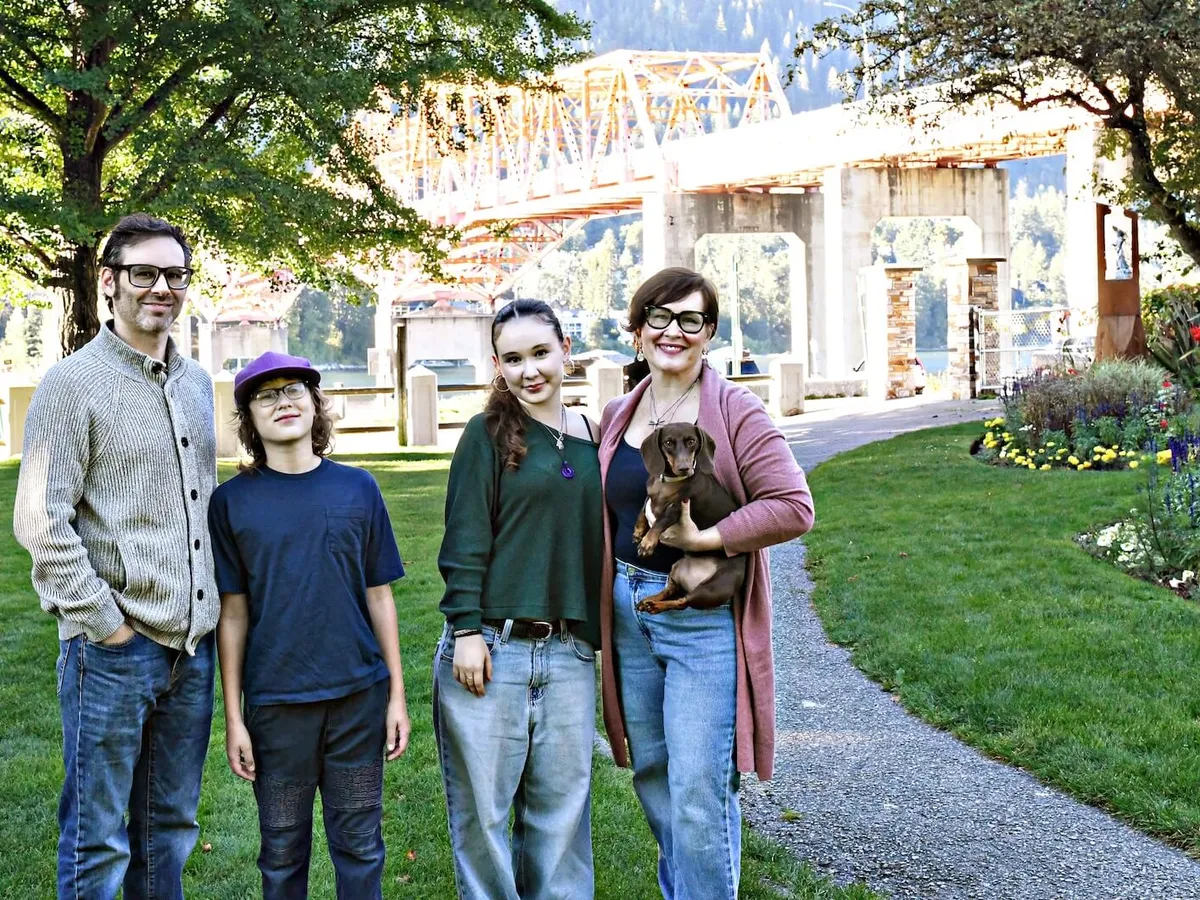 Jess Phillips's family in Nelson in 2026: her husband, their two children now teenagers, and Jess holding the family dog, by the same bridge
